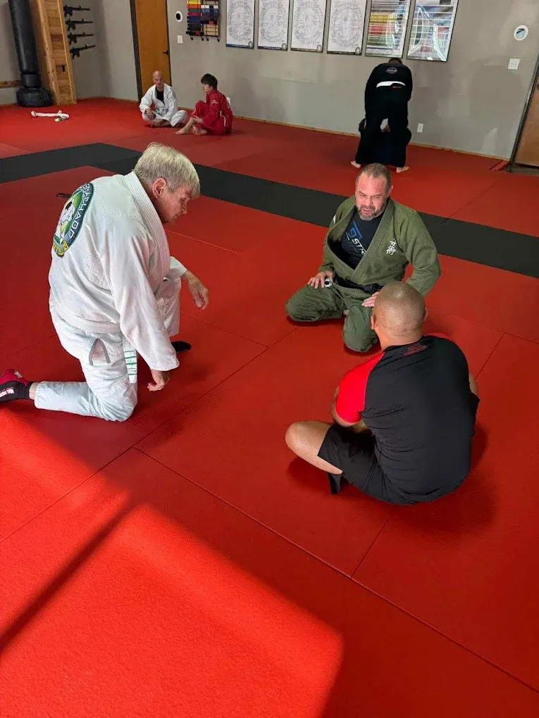 An instructor walking two adult students through a technique on the mat during Brazilian Jiu-Jitsu class at Davis Martial Arts & Fitness in Pilot Point, TX