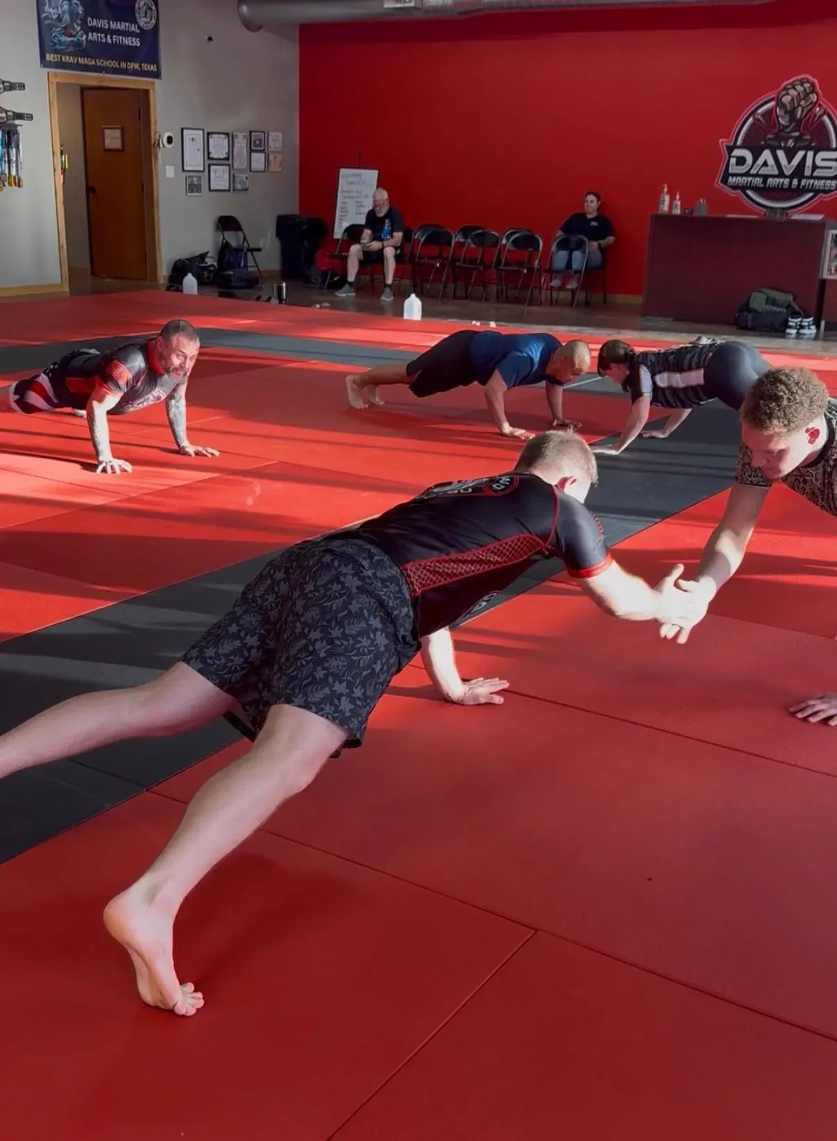 Adult students holding a plank during a partner conditioning drill on the mats at Davis Martial Arts & Fitness