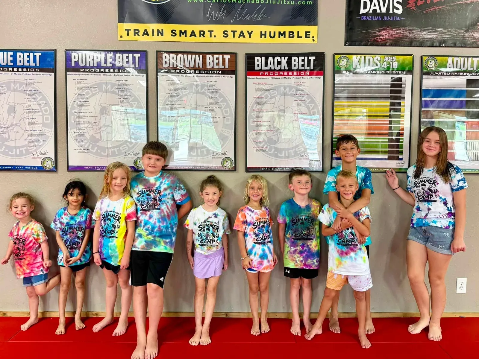 A group of summer camp kids standing together in front of the belt progression wall at Davis Martial Arts & Fitness in Pilot Point, TX