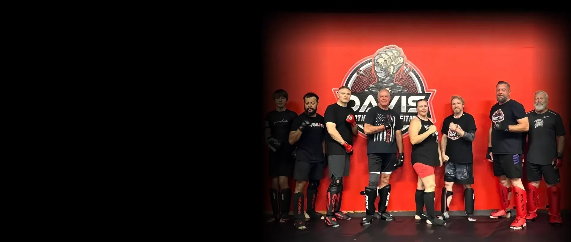 Kickboxing group posing at the red Davis logo wall at Davis Martial Arts & Fitness in Pilot Point, TX