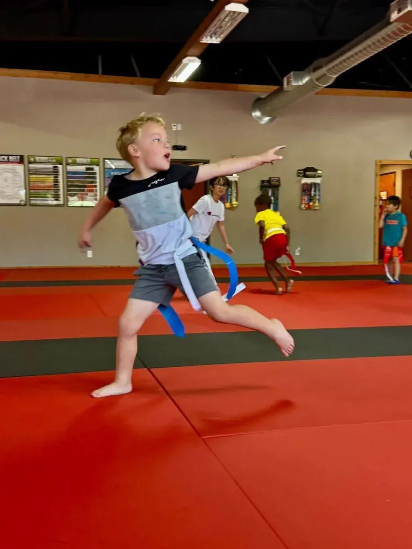 A summer camp boy sprinting across the red mats mid-flag-tag game with flags hanging from his belt at Davis Martial Arts & Fitness