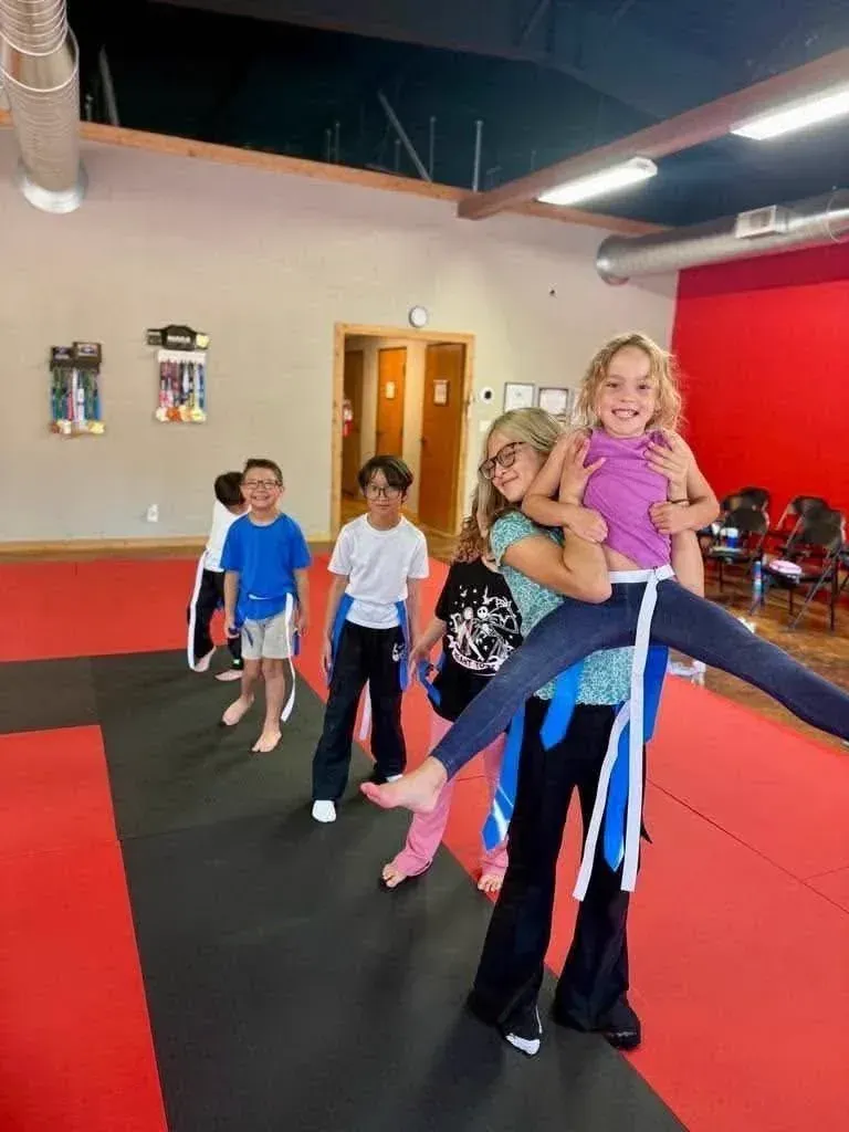 Summer camp kids wearing flag belts on the mats while one camper kicks a leg high during a game at Davis Martial Arts & Fitness