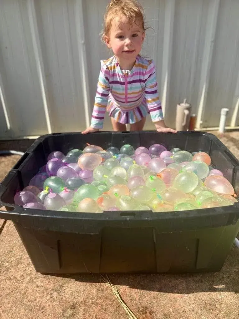 A small summer camper leaning over a tub filled with water balloons outside Davis Martial Arts & Fitness