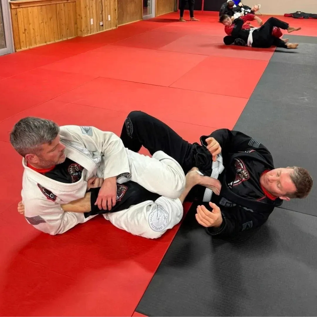 Two adults sparring Brazilian Jiu-Jitsu in gis on the red mat at Davis Martial Arts & Fitness in Pilot Point, TX
