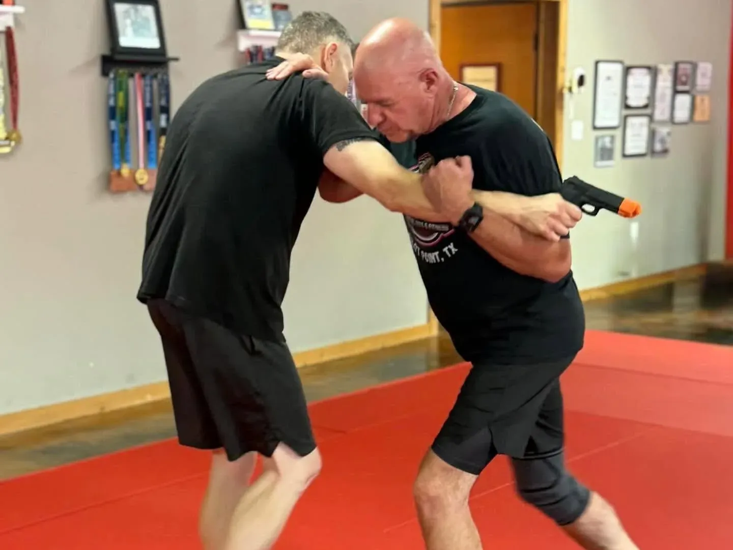 An instructor drilling a Krav Maga handgun-disarm from behind with a training pistol at Davis Martial Arts & Fitness in Pilot Point, TX